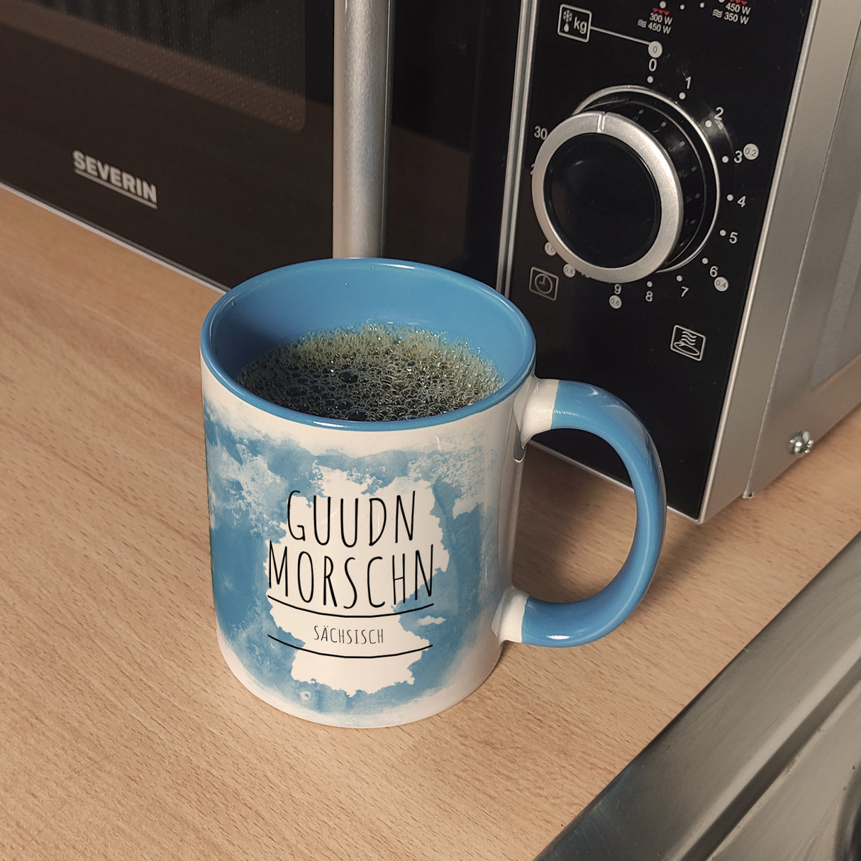 Hallo auf Sächsisch Guudn Morschen lustiger Kaffeebecher mit blauem Hintergrund