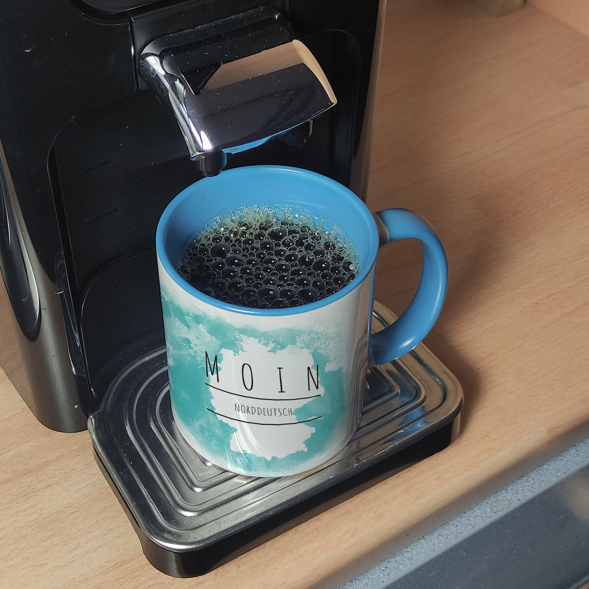 Hallo auf Norddeutsch Moin lustiger Kaffeebecher mit blauem Hintergrund