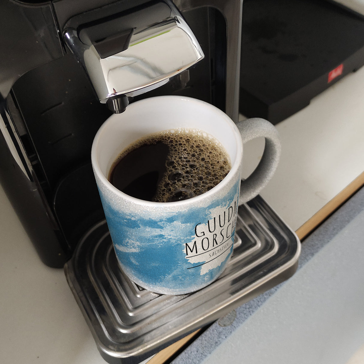 Hallo auf Sächsisch Guudn Morschen lustiger Kaffeebecher mit blauem Hintergrund