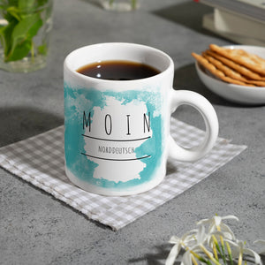 Hallo auf Norddeutsch Moin lustiger Kaffeebecher mit blauem Hintergrund